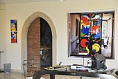 Wohnraum mit Designertisch aus Metall, Wandkunstwerken & Blick durch Holztür in Badezimmer