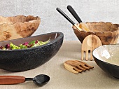 Wood and stone bowls with salad servers on a light surface