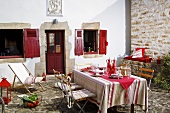 Gedeckter Tisch auf Terrasse vor Haus mit roter Tür & roten Fensterläden