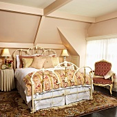 Schlafzimmer mit Metall-Doppelbett, antikem Polsterstuhl & Teppich