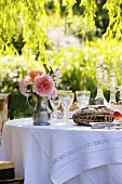 Gedeckter Tisch mit Brot, Weingläsern und Rosenstrauss im Garten