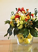 Flower arrangement in a glass vase filled with apples
