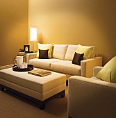 Beleuchtetes Wohnzimmer mit Sofa, Sessel & Polsterhocker als Couchtisch