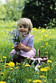 Kleines Mädchen hält Blumen neben Korb mit Ostereiern