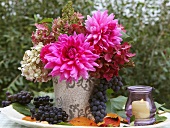 An autumnal bouquet of dahlias with grapes and lanterns on a garden table