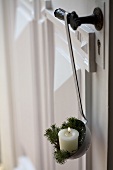 Candle and white spruce twigs in enamel ladle on door handle