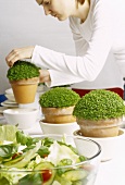 Young woman arranging potted plants on a table with salad