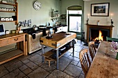 Ländliche Küche mit Steinboden, Hackstock, Esstisch und Kaminfeuer