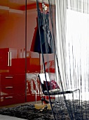 Blick durch transparenten Vorhang auf roten Kleiderschrank, Stuhl & Flokati eines Schlafzimmers