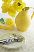 Yellow tulips in a jug with cutlery on a plate
