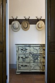 Open doorway with a view to hats on wall hooks and painted chest of drawers
