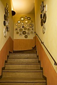 Treppenhaus mit Holztreppe und Spiegelsammlung an gelber Wand