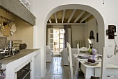 An open-plan dining room with a kitchen and view through an archway into a living room with a wood beamed ceiling