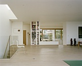 A modern, open plan living room with a parquet floor, chairs in front of a glass balustrade and a built in bookshelf