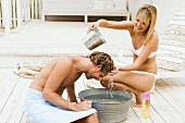 Woman washing man's hair over tub of water