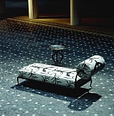 A chaiselongue in the middle of a large reception room on a blue patterned floor