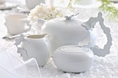 A white tea pot with a sugar bowl and a milk jug on a white table cloth