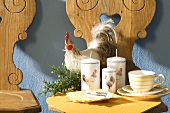A stuffed cockerel, candles and breakfast crockery on a kitchen stool