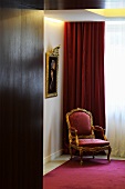 A baroque armchair with a red upholstery in front of a velvet curtain in the corner of a room