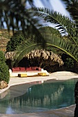 A pool under palms trees and a couch in the courtyard of a dammuso (Pantelleria, Sicily, Italy)
