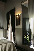 Marokkanisches Schlafzimmer mit Bett, bodenlangen Fenstervorhängen & orientalischer Wandlampe