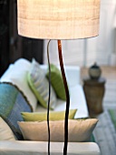 Floor lamp wit light colored shade in front of a sofa