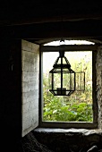 Lantern in a open window hanging on a lintel with wooden shutters on the inside and a view onto a garden