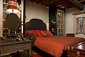 Bed with upholstered headboard and red bed linen in a bedroom in a country home