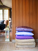 Stack of pillows with shiny silk fabric in front of a brown wood paneled wall next to a passage with a view into the living room