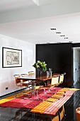 A dining table against a black wall with cantilever chairs on a red striped rug on a black floor
