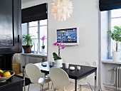 A black dining table with white Bauhaus chairs and a TV on the wall