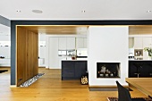 Open plan kitchen with fireplace in front of a black kitchen unit and white built in cupboard