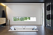 A sunken bathtub in a designer bathroom with a window opening and indirect lighting