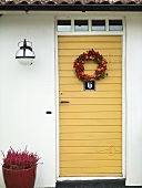 A yellow door hung with a wreath of berries