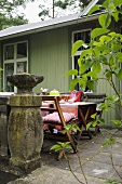 Gedeckter Tisch auf Steinterrasse vor grünem Holzhaus