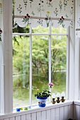 Fenster mit geblümter Vorhangblende und Blick in Garten