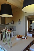 Black lampshades above a dining table with flower vases and a fruit bowl