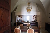 A view into a dining room in front of a kitchen oven with an extraction hood and a chandelier hanging from a vaulted ceiling
