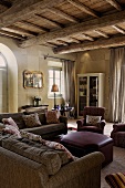 Living room in a country home with a rustic beam ceiling, beneath a cozy sitting room with leather ottomans