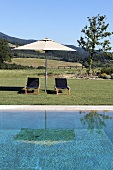 Relaxing by the pool with lounge chairs under a sun umbrella and view of the Mediterranean countryside