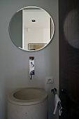 Round bathroom mirror above a cylindrical stone vanity and chrome wall fittings in designer style