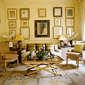 A living room in a period building with a coffee table, a sofa and an armchair in front of a collection of pictures