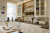 weiße Landhausküche mit Vitrinenschränken und Tellerboard und einem Küchenblock
