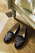 Black embroidered slippers in a bedroom with a wooden floor