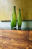 Grüne Vasen auf Holzsideboard vor gelbem Bild