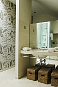 An open wash area - baskets under a wash basin in front of a mirror and a partition wall to the side