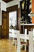 A wood panelled dining room with a white designer table and white designer chairs and a view through the open double doors onto the sculptures in the hallway