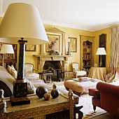 Upholstered furniture in front of a fireplace and a table lamp with a white shade on a side table in a living room with yellow walls