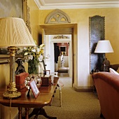 Table lamps with plissee shades on a wall table in a yellow-painted living room with a view into a corridor