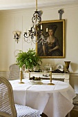 Brass candle sticks on a dining table laid with a white cloth and a chandelier with glass bead decoration